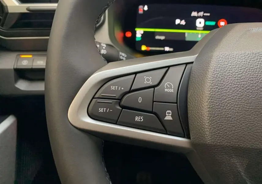 Gros plan sur les commandes au volant cuir du DACIA BIGSTER Hybrid 155 Journey Plus avec tableau de bord digital en arrière-plan.