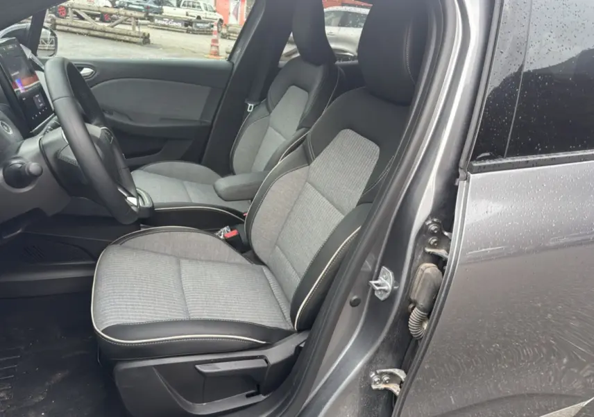 Vue intérieure côté conducteur de la Renault Clio gris schiste 2025, montrant les sièges avant en tissu et cuir avec volant multifonctions.