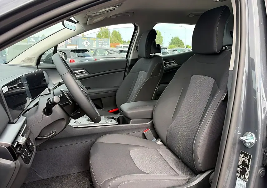 Vue intérieure côté conducteur du Kia Sportage 1.6 hybride gris eclipse, avec sièges tissu et accoudoir central.