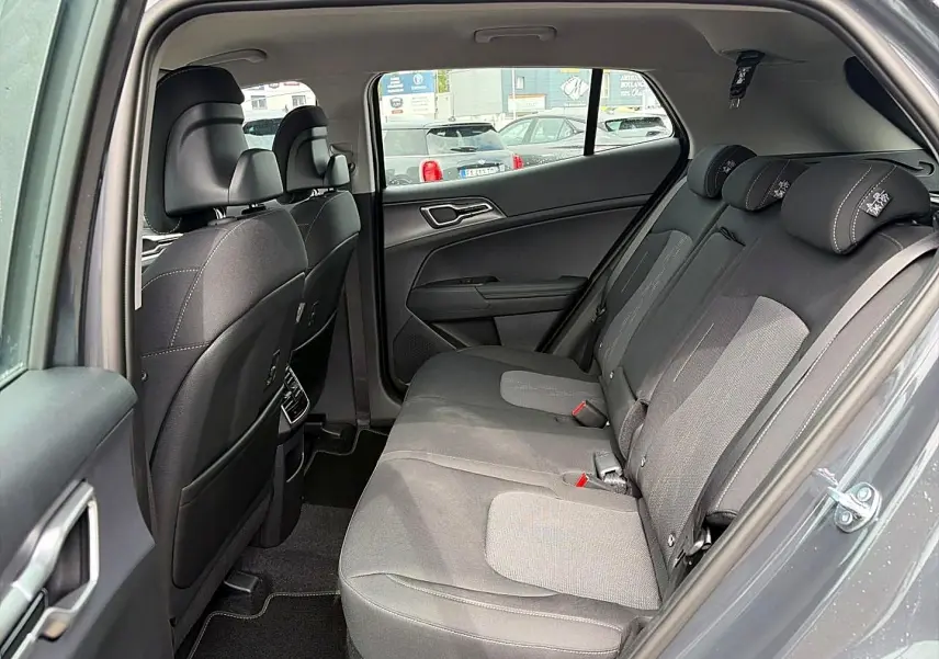 Vue intérieure côté droit des sièges arrière gris du Kia Sportage 1.6 hybride 239 active avec appuie-têtes et ceintures visibles.