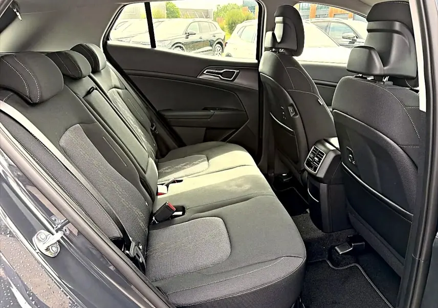 Vue intérieure côté gauche montrant la banquette arrière grise et les sièges avant du Kia Sportage 1.6 hybride 2026.