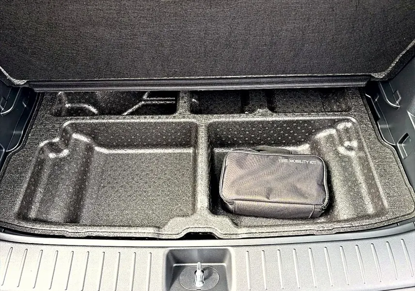 Coffre ouvert du Kia Sportage 1.6 hybride gris eclipse, vue du compartiment de rangement avec kit de mobilité pneus.