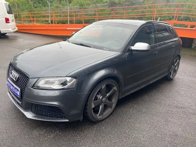 Audi RS3 Sportback gris Daytona vue 3/4 avant droit, jantes noires et coques de rétroviseurs argentées.