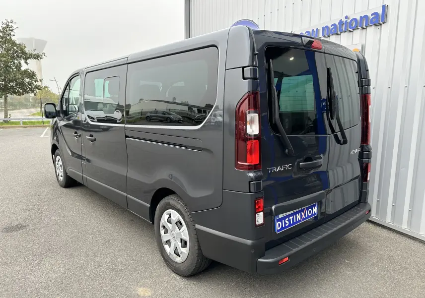 Renault Trafic Combi gris comète vu en 3/4 arrière droit, soulignant ses grandes vitres teintées et portes arrière battantes.