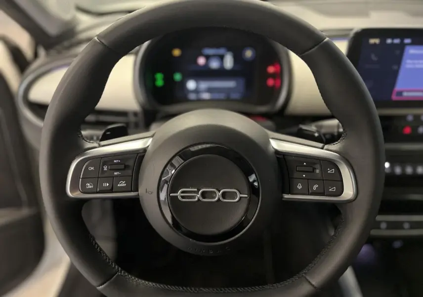 Volant noir avec logo 600 chromé au centre, planche de bord ivoire et écran numérique du Fiat 600 hybride 2024.