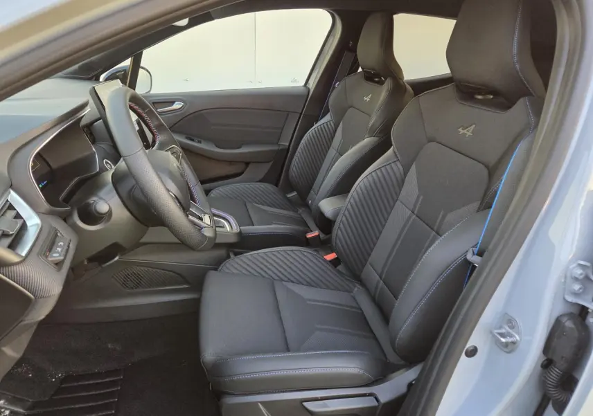 Intérieur avant de la Renault Clio V hybride, sièges sport noirs avec surpiqûres bleues et logo Alpine visibles côté droit.