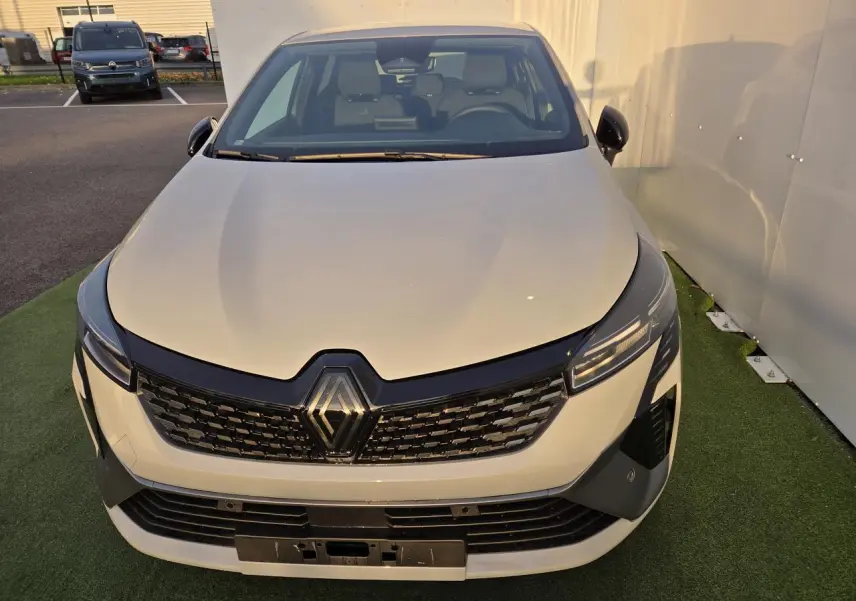 Vue avant rapprochée d'une Renault Clio V hybride gris Rafale avec calandre noire et phares LED fins.