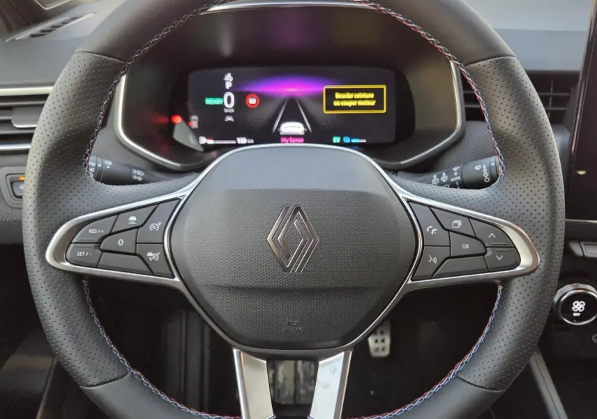 Vue rapprochée du volant perforé noir avec surpiqûres tricolores et logo Renault au centre du tableau de bord numérique.