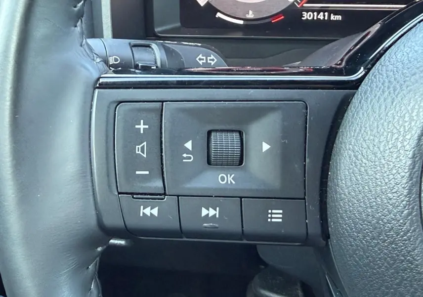 Gros plan sur les commandes multifonctions à gauche du volant cuir du Nissan Qashqai rouge 2022, avec écran numérique partiel visible.