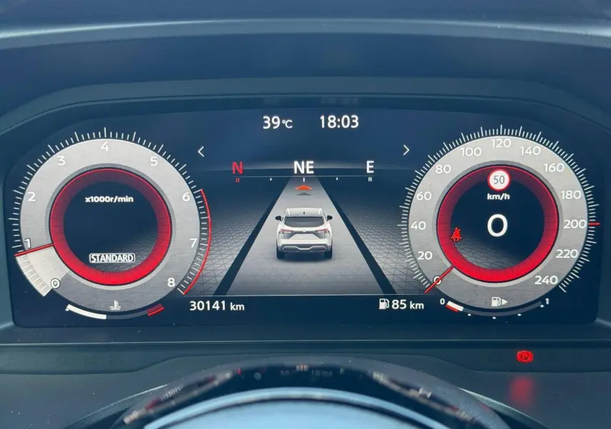 Tableau de bord numérique du Nissan Qashqai 2022 affichant la vitesse, le compte-tours et une vue arrière du véhicule blanc.