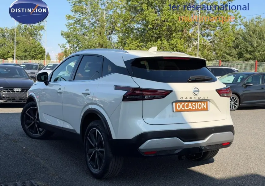 Vue 3/4 arrière gauche d'un Nissan Qashqai blanc avec jantes noires et attelage de remorque visible.