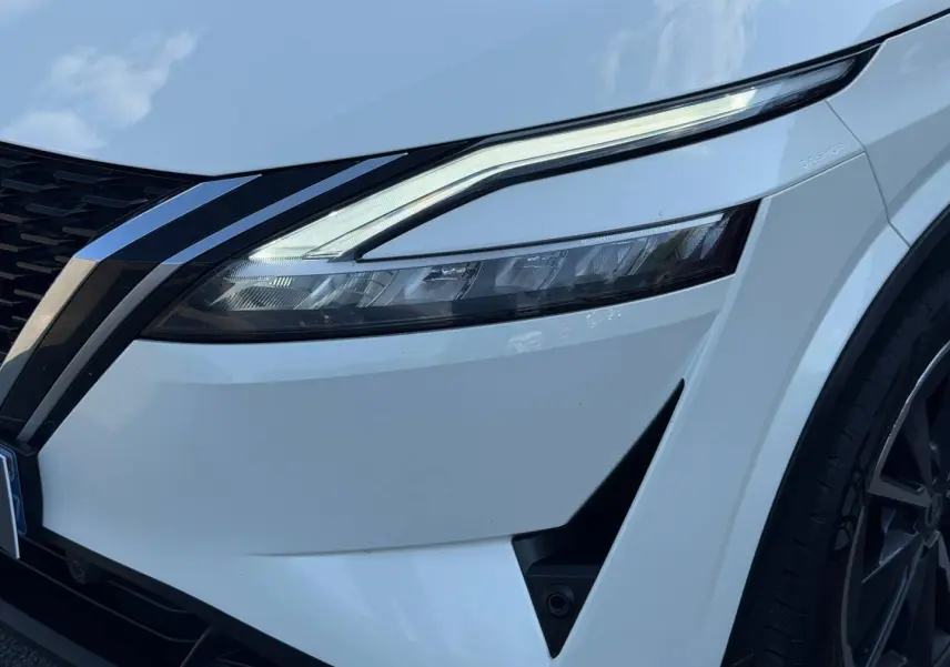 Gros plan sur l'avant droit blanc du Nissan Qashqai 2022, mettant en valeur le phare LED et la calandre noire.