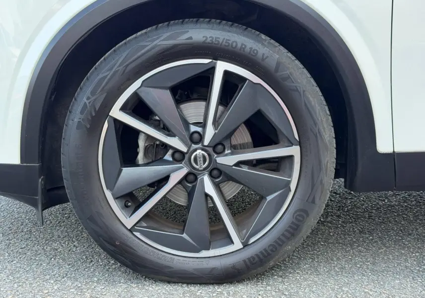 Gros plan sur la roue avant droite d’un Nissan Qashqai blanc avec jante alliage noire et argentée.