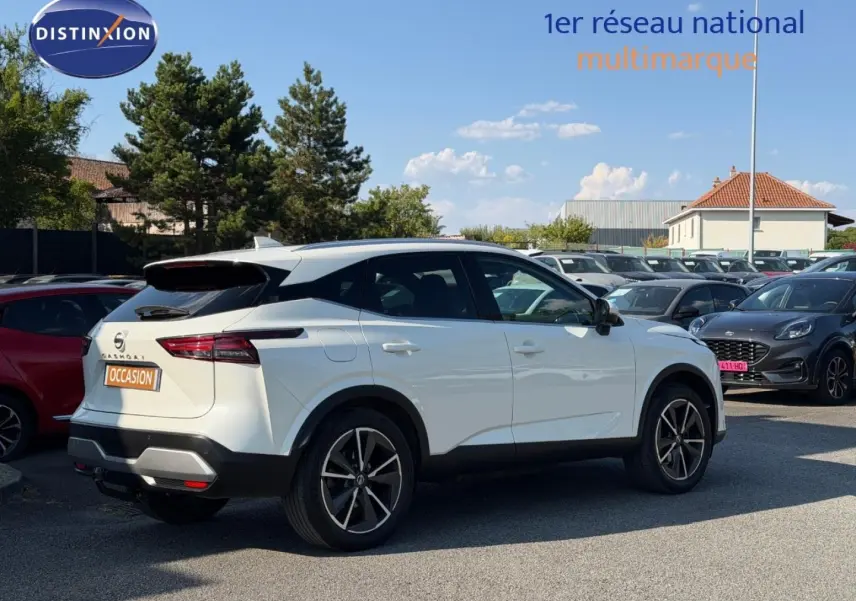 Nissan Qashqai blanc en 3/4 arrière droit sur parking, avec jantes alliage et feux arrière LED distinctifs.