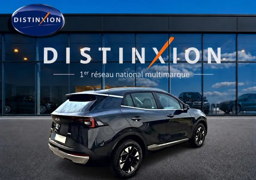Vue 3/4 arrière droite d'un KIA SPORTAGE 1.6 hybride gris eclipse avec jantes alu et feux arrière LED, devant une vitrine Distinxion.