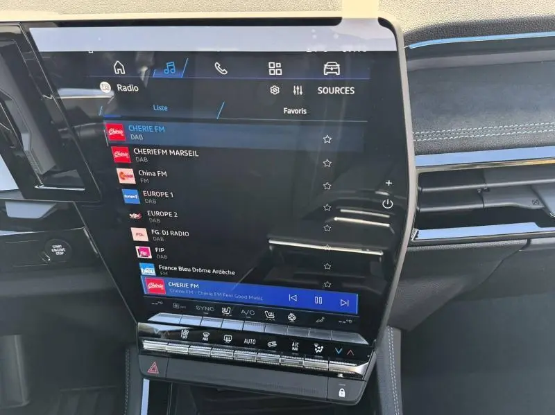Écran tactile central du tableau de bord du Renault Austral blanc nacré, avec interface radio et commandes climatisation visibles.