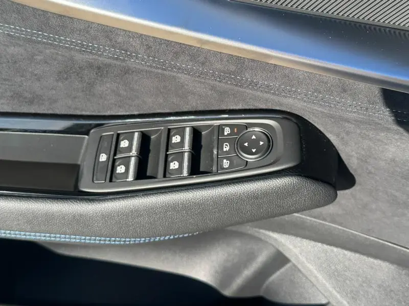 Gros plan sur les commandes de lève-vitres et rétroviseurs noirs sur la porte intérieure en tissu carbone et Alcantara bleu du Renault Austral blanc nacré.