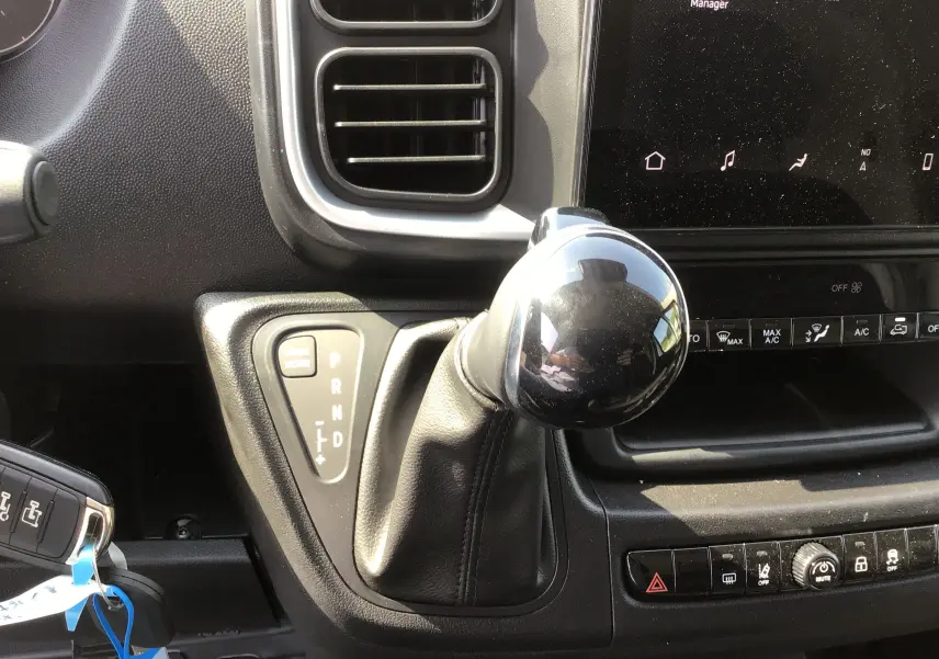 Gros plan sur le levier de vitesses automatique noir du Peugeot Boxer Fourgon gris, avec tableau de bord et écran tactile visibles.