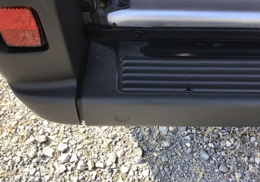 Gros plan sur le pare-chocs arrière noir avec feu rouge du Peugeot Boxer Fourgon gris Artense, détail du capteur de recul visible.