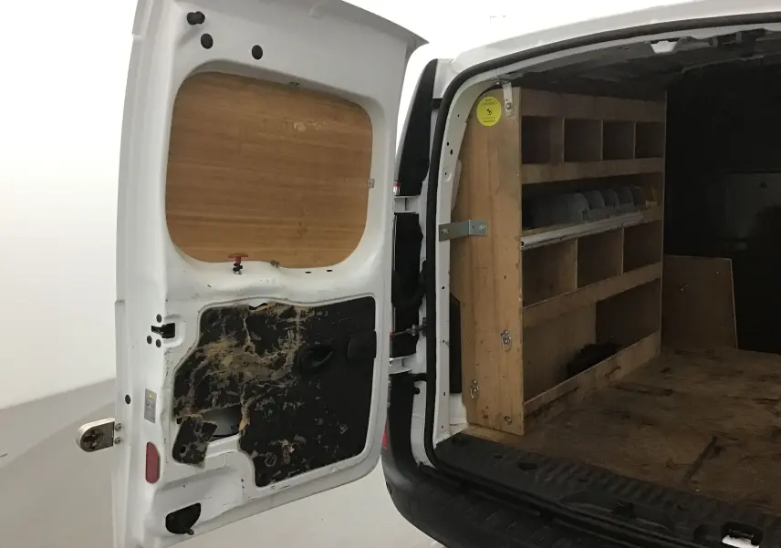 Vue arrière ouverte du Renault Kangoo blanc 2021 montrant l'aménagement bois intérieur avec étagères de rangement.