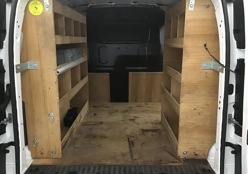 Vue arrière du Renault Kangoo blanc 2021 montrant l'intérieur utilitaire avec étagères en bois et plancher usé.