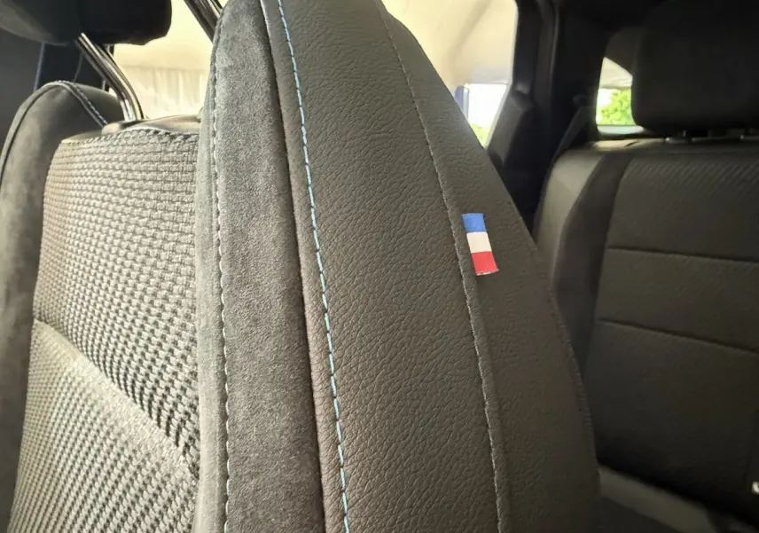 Gros plan sur le siège avant droit gris foncé du Renault Espace esprit Alpine 2025 avec surpiqûres bleues et drapeau tricolore.