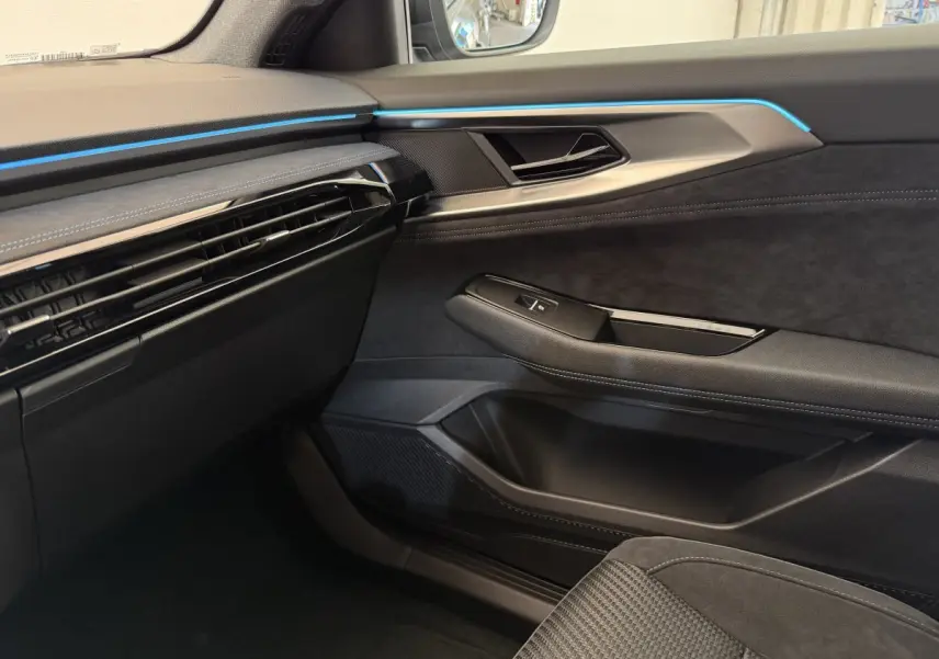 Intérieur côté passager du Renault Espace gris foncé 2025, avec éclairage d'ambiance bleu et garnitures noires élégantes.