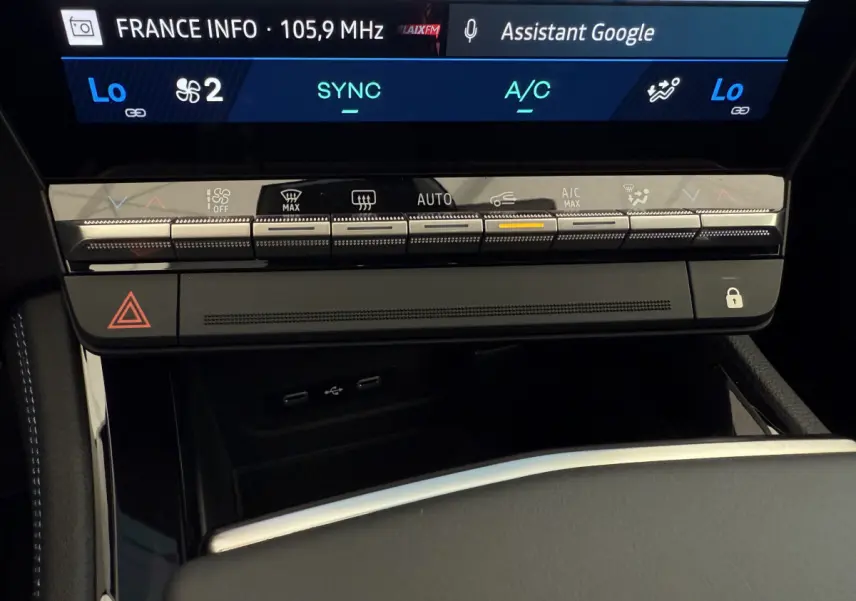 Gros plan sur la console centrale de la Renault Espace gris foncé, avec commandes climatisation et écran tactile affichant radio et assistant Google.