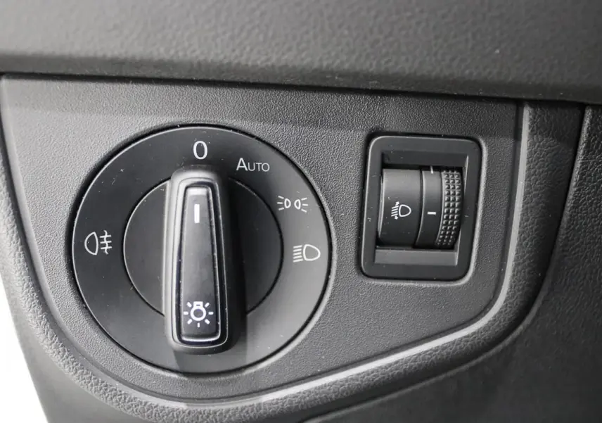 Gros plan sur la molette de réglage des phares et le variateur d'intensité lumineuse du tableau de bord d'une Volkswagen Polo blanche.