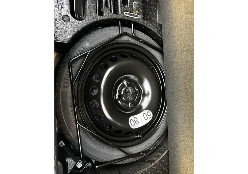 Roue de secours noire avec étiquette de limitation 80 km/h dans le coffre d'une Renault Clio gris schiste.