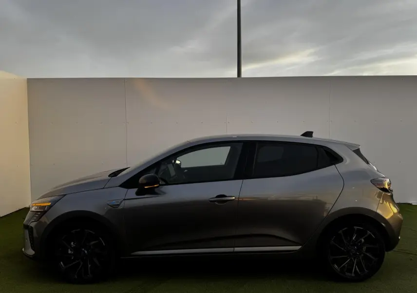 Profil côté gauche d'une Renault Clio V hybride gris schiste avec jantes noires et vitres surteintées.