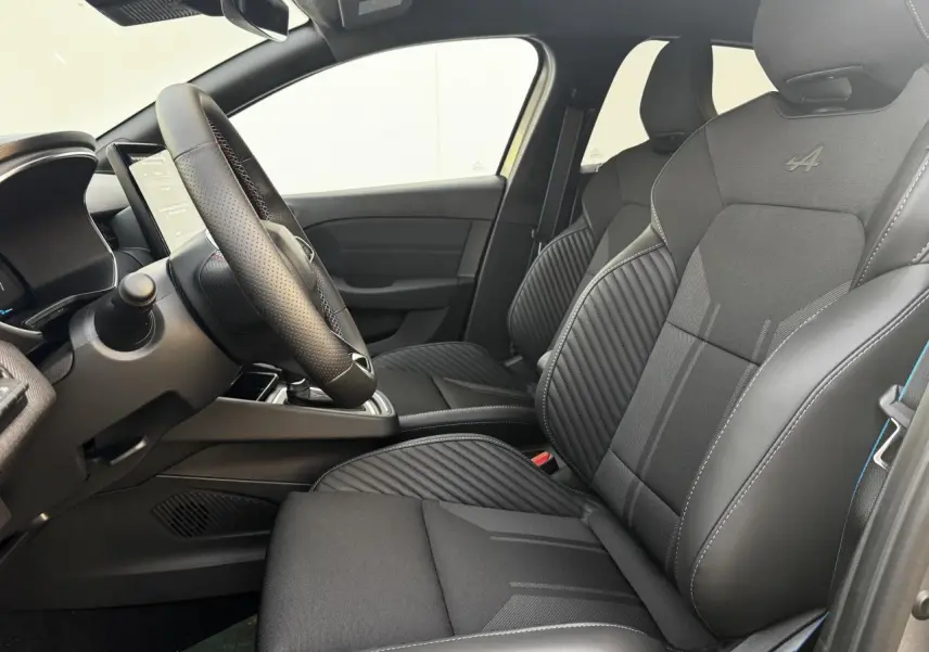 Intérieur avant droit de la Renault Clio V hybride, sièges sport noirs avec logo Alpine brodé et surpiqûres bleues.