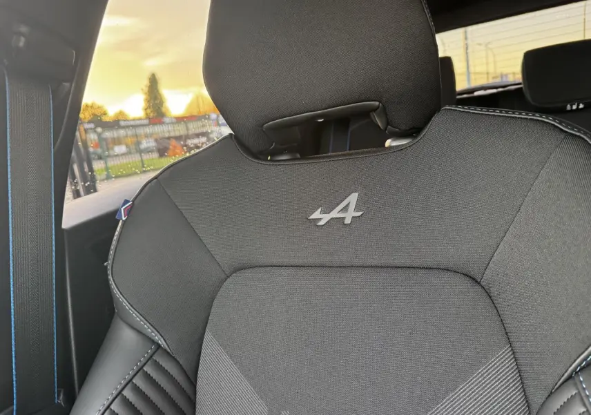 Gros plan sur le siège avant noir avec logo Alpine et surpiqûres bleues dans une Renault Clio Gris Schiste Métal.