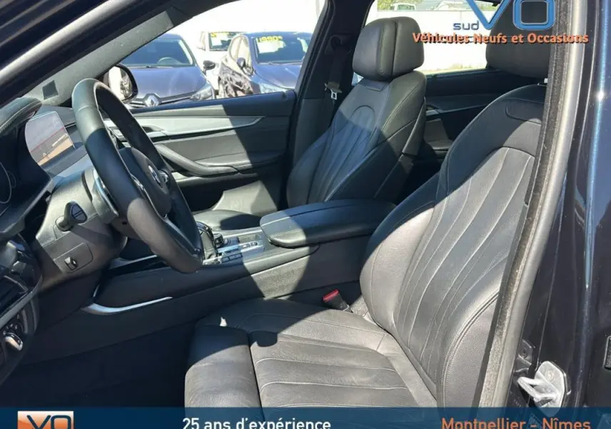 Vue intérieure côté conducteur du BMW X6 F16 noir avec sièges cuir et accoudoir central visible au soleil.