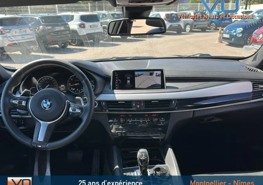 Intérieur BMW X6 F16 noir vu de face, volant sport cuir, écran GPS affichant caméra de recul, tableau de bord moderne.