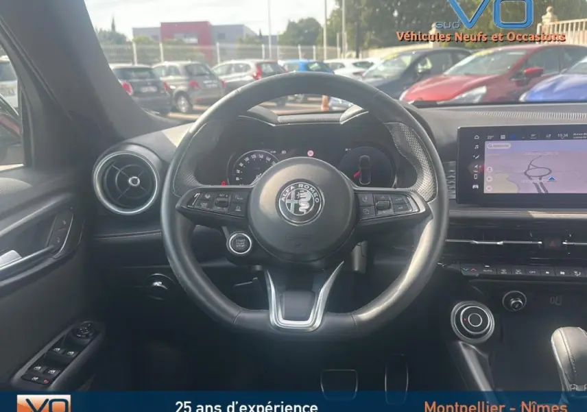 Vue centrée sur le volant sport de l'Alfa Romeo Tonale rouge 2024, avec tableau de bord et écran tactile visibles.