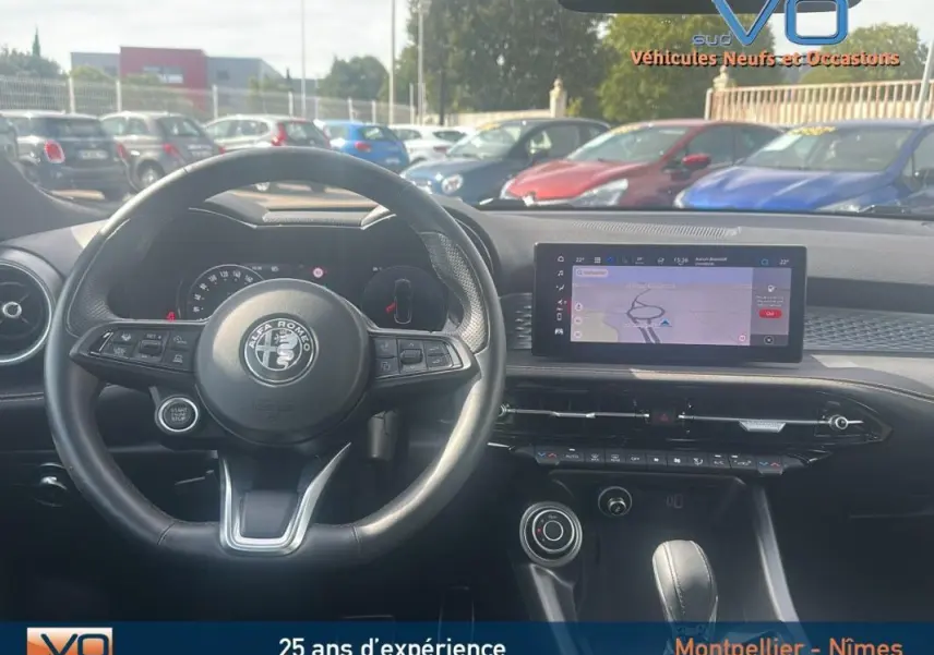 Vue intérieure centrée sur le volant sport et l'écran tactile du tableau de bord de l'Alfa Romeo Tonale rouge 2024.