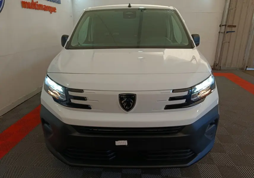 Vue avant d'un Peugeot Partner blanc 2026 avec phares allumés et calandre noire distinctive.