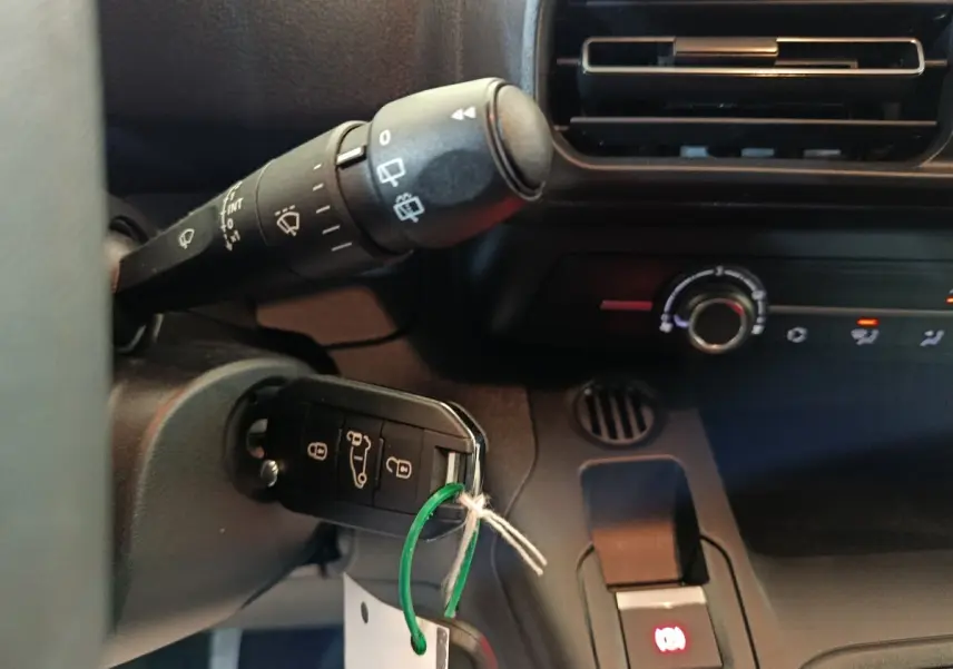 Gros plan intérieur sur le tableau de bord du Peugeot Partner blanc 2026, montrant la clé insérée et les commandes de climatisation.