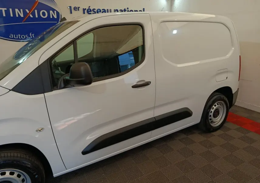 Vue de profil côté gauche du Peugeot Partner blanc 2026 avec porte latérale pleine et protections noires sur porte.