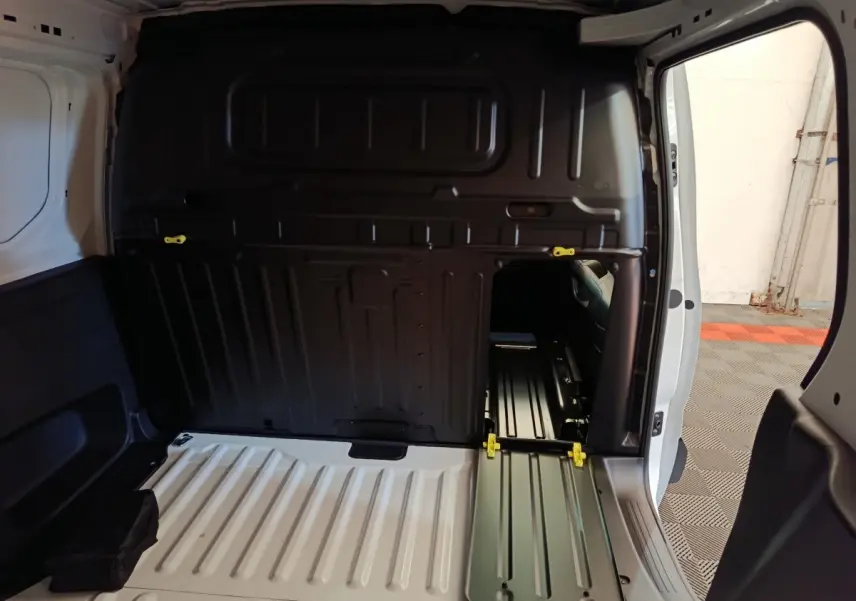 Vue intérieure arrière du Peugeot Partner blanc, montrant la cloison pleine avec trappe d'accès et plancher de chargement métallique.