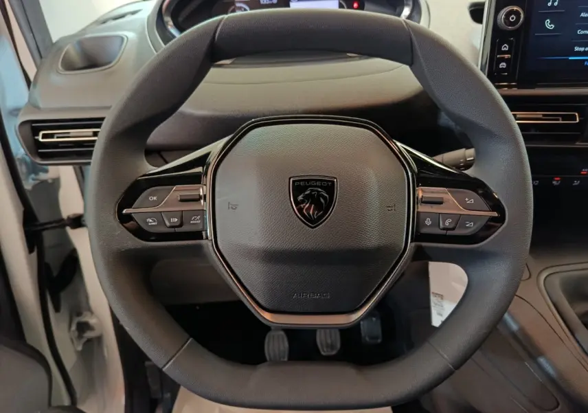 Vue rapprochée du volant noir du Peugeot Partner 2026 avec commandes intégrées et tableau de bord partiellement visible.