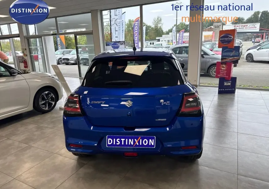 Vue arrière d'une Suzuki Swift 1.2 Pack Hybrid bleu exposée en showroom avec feux arrière fumés et logo distinctif.