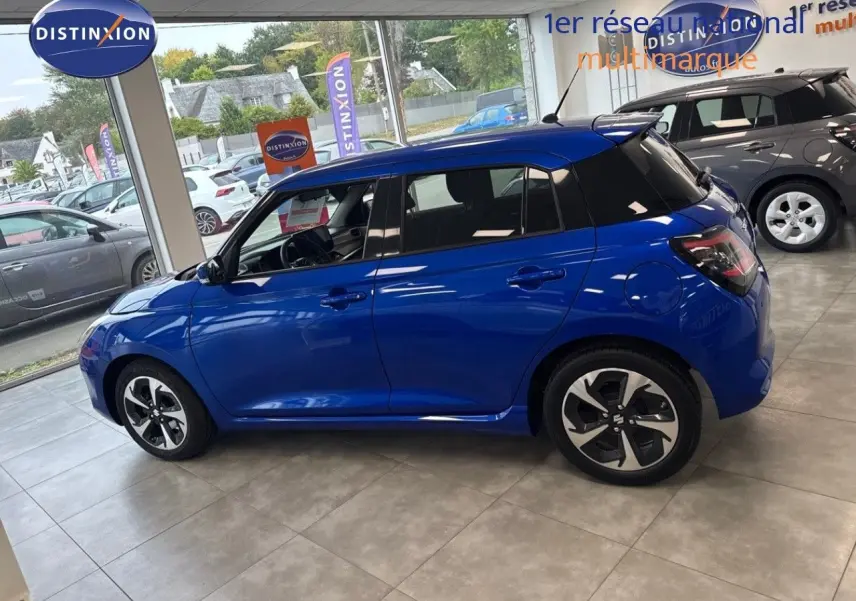 Vue de profil côté gauche d'une Suzuki Swift 1.2 Pack Hybrid bleu, en showroom avec jantes distinctives noires et argent.