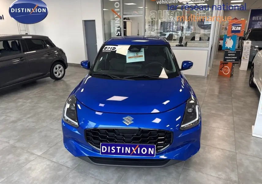 Vue avant d'une Suzuki Swift 1.2 Pack Hybrid bleu brillant exposée en showroom avec calandre noire et phares LED.