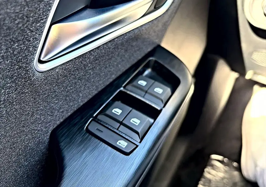Gros plan sur les commandes des vitres électriques côté gauche d’une MG ZS noire, avec poignée de porte argentée.