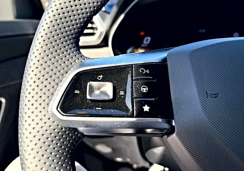 Gros plan sur les commandes multifonctions à gauche du volant perforé noir du MG Motor ZS 1.5 hybrid 197 standard.