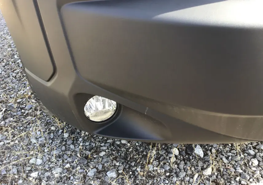 Gros plan sur le projecteur antibrouillard avant droit du Peugeot Boxer Fourgon gris Artense posé sur un sol gravillonné.