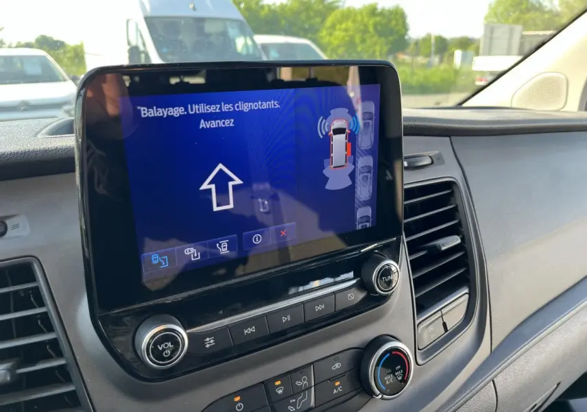 Vue rapprochée de l'écran tactile central du Ford Transit Custom blanc, affichant l'assistance au stationnement active.