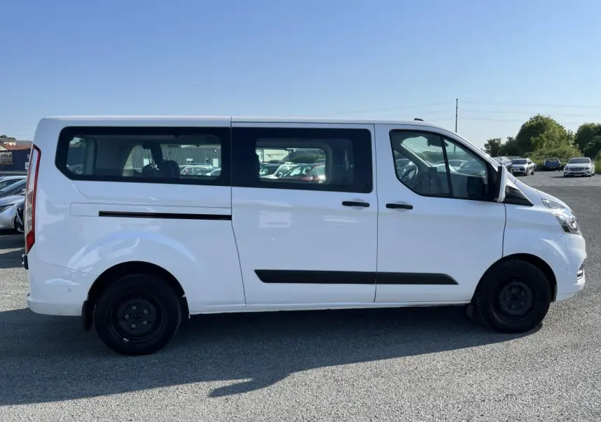 Profil côté droit d'un Ford Transit Custom Kombi blanc, avec vitres latérales teintées et jantes acier noires.